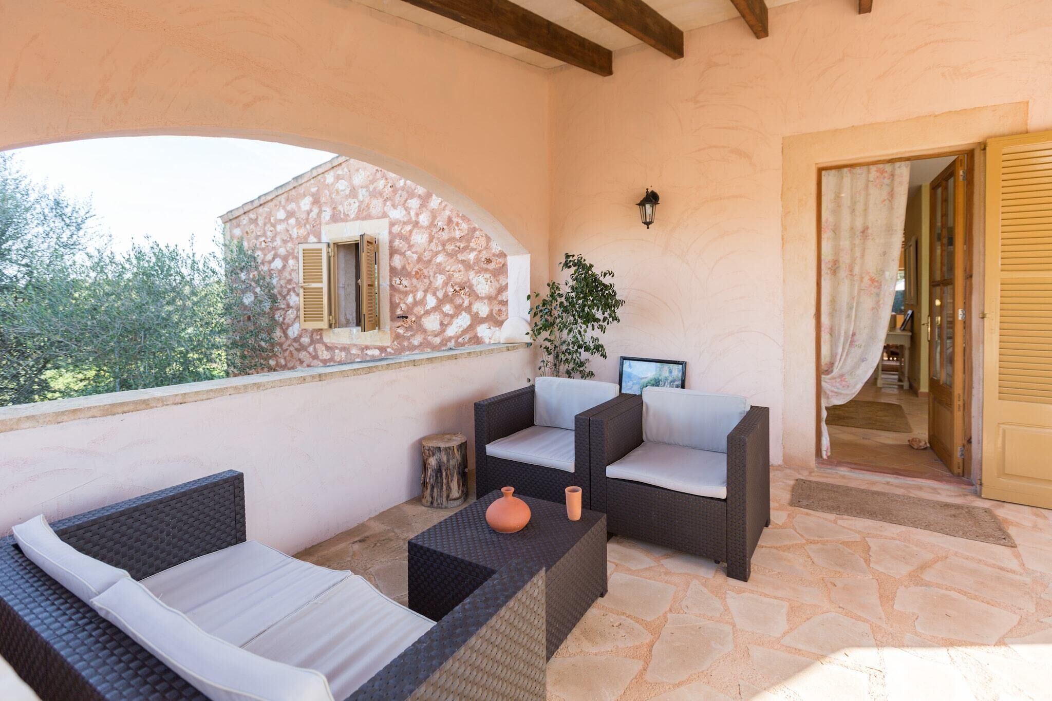 A balcony with wicker furniture, a stone wall, and a view of a building with shutters.