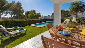 Une terrasse avec une piscine, une table à manger mise pour le petit-déjeuner et des chaises longues.