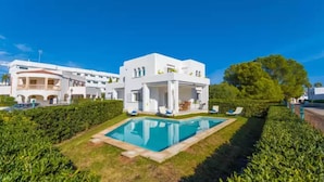 Une villa blanche dotée d’une piscine, entourée de haies bien entretenues et d’un grand arbre.