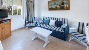 Een woonkamer met een gestreepte bank, een witte salontafel en een televisie op een houten kast.