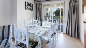 Een eethoek met een tafel voor vier personen, witte stoelen, een fles rode wijn en een lijst met een afbeelding aan de muur.