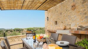 An outdoor dining area with wicker chairs and a table set for a meal, overlooking a scenic landscape.