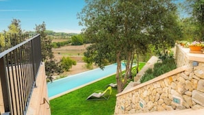 A balcony with a stone wall, a pool, and a view of a green landscape.