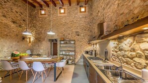 A rustic kitchen with stone walls, a wooden dining table with chairs, and stainless steel appliances.