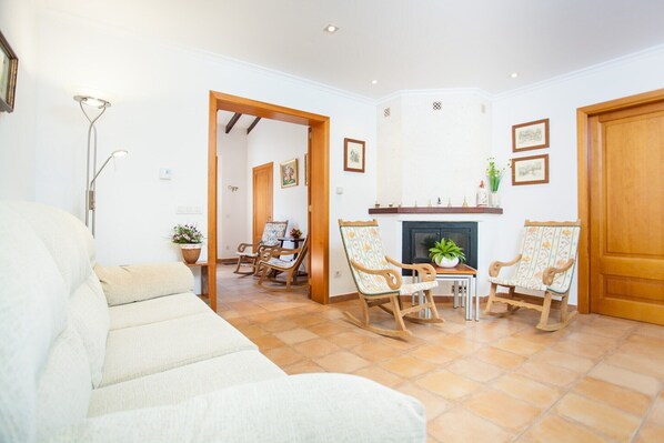 A living room with a sofa, wooden rocking chairs, a fireplace, and a dining area with a table and chairs.