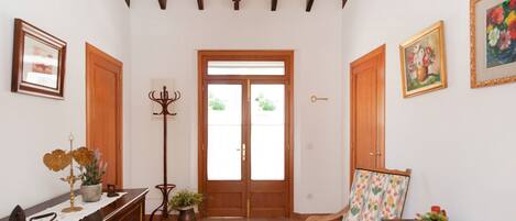 A hallway with wooden doors, a large window, a coat rack, a chair, and a table with a vase.