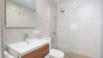 A modern bathroom with a white sink, a wooden vanity, a toilet, and a glass-enclosed shower area.