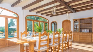Un comedor con mesas y sillas de madera, ventanas amplias y un aparador de madera.