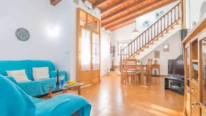 A spacious living area with a blue sofa, a dining table, and a staircase leading to an upper floor. - Sa Tanqueta De Ses Roques - Villa With Pool (Santanyí, Illes Balears)