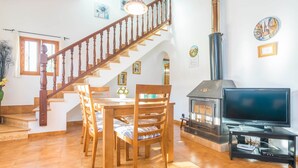 A living room with a wooden staircase, a fireplace, a television on a stand, and a dining table with chairs. - Sa Tanqueta De Ses Roques - Villa With Pool (Santanyí, Illes Balears)
