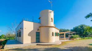 A modern building with a cylindrical tower, a covered outdoor area, and a gravel pathway. - Sa Tanqueta De Ses Roques - Villa With Pool (Santanyí, Illes Balears)
