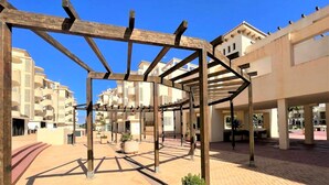 A covered outdoor area with a wooden pergola structure, potted plants, and a paved walkway.