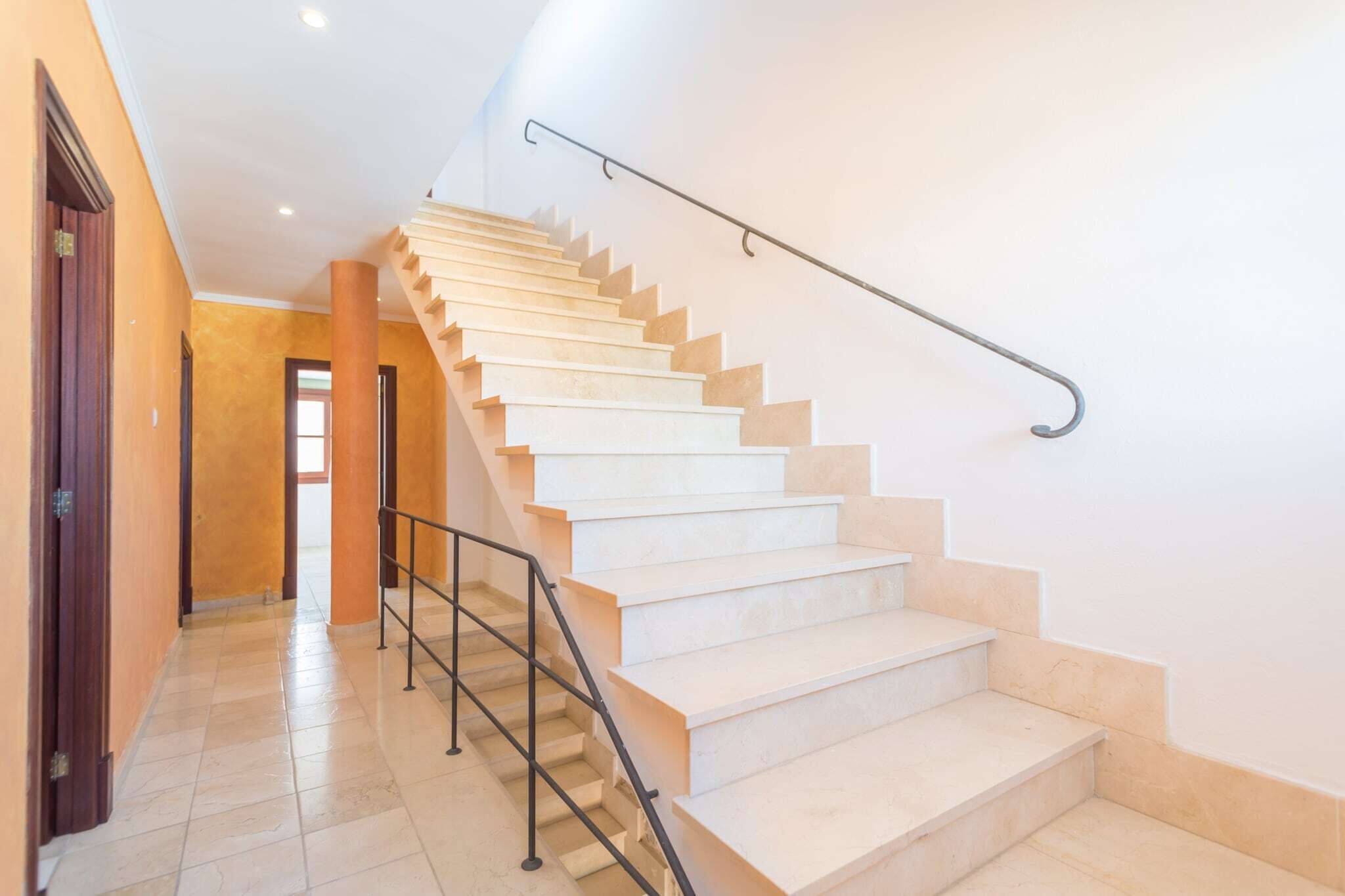 Una escalera con barandilla metálica, escalones color beige y pared de tono claro.