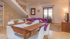 Una sala de estar moderna con una mesa de comedor de madera, sillas blancas, un sofá morado y una escalera con pared de piedra.