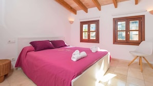 Un dormitorio con una cama, dos ventanas, una silla y una mesita.