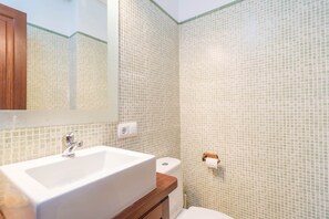 Un baño con lavamanos blanco, un armario de madera, un inodoro y un espejo.