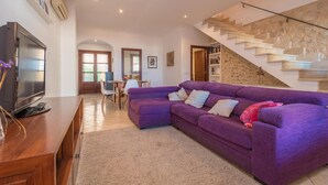 Una sala de estar con un sofá púrpura, un mueble de televisión de madera y una escalera con escalones de piedra.
