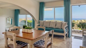 A room with a dining table, chairs, a sofa, and a view of the sea. - Pano Stalos (Chania)