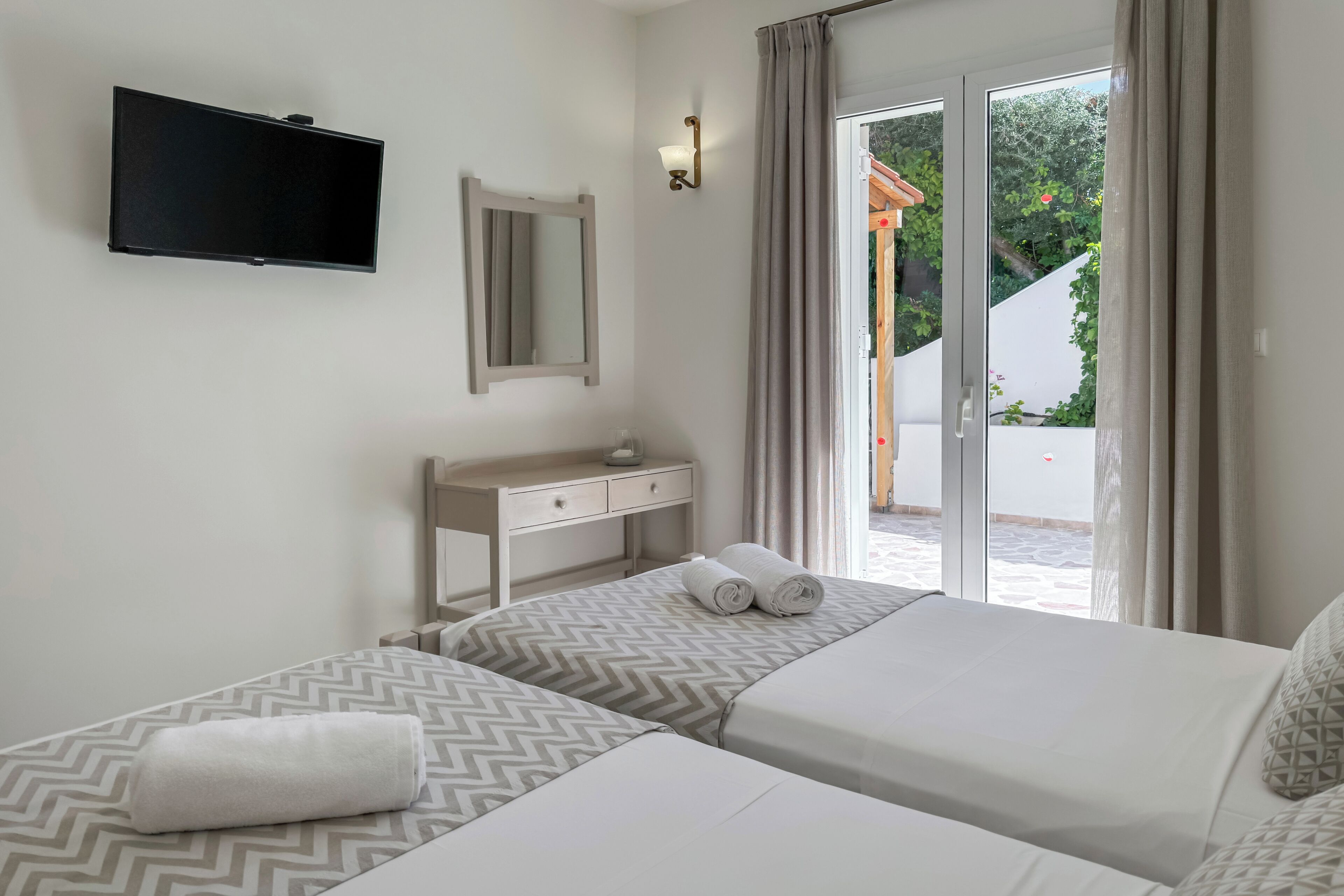 Een hotelkamer met twee bedden, een televisie, een bureau en een glazen schuifdeur naar buiten.