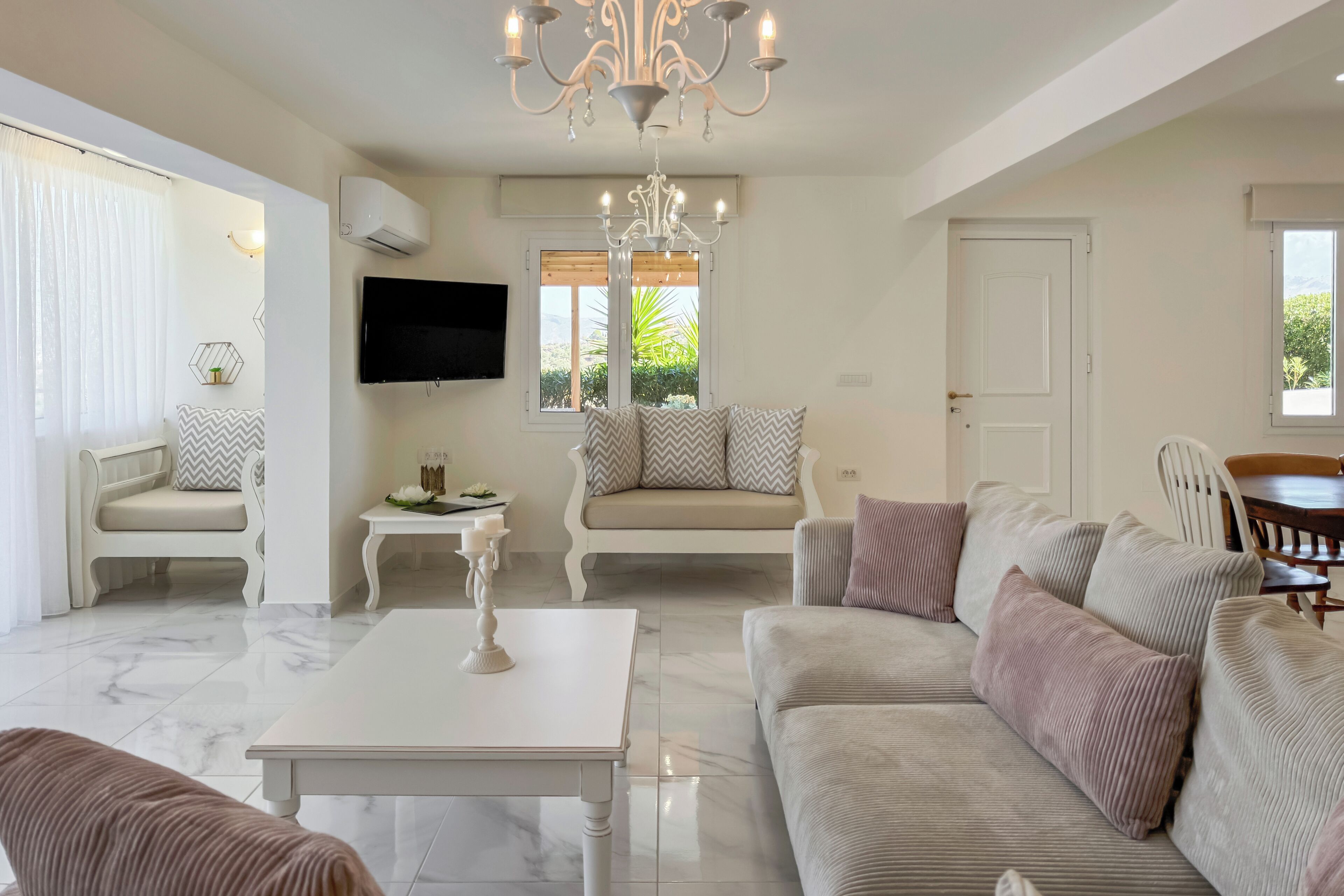 A spacious living room with a white sofa, a beige sofa, a coffee table, and a chandelier.