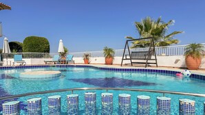 A swimming pool with blue-tiled edges, lounge chairs, and palm trees. - Pano Stalos (Chania)