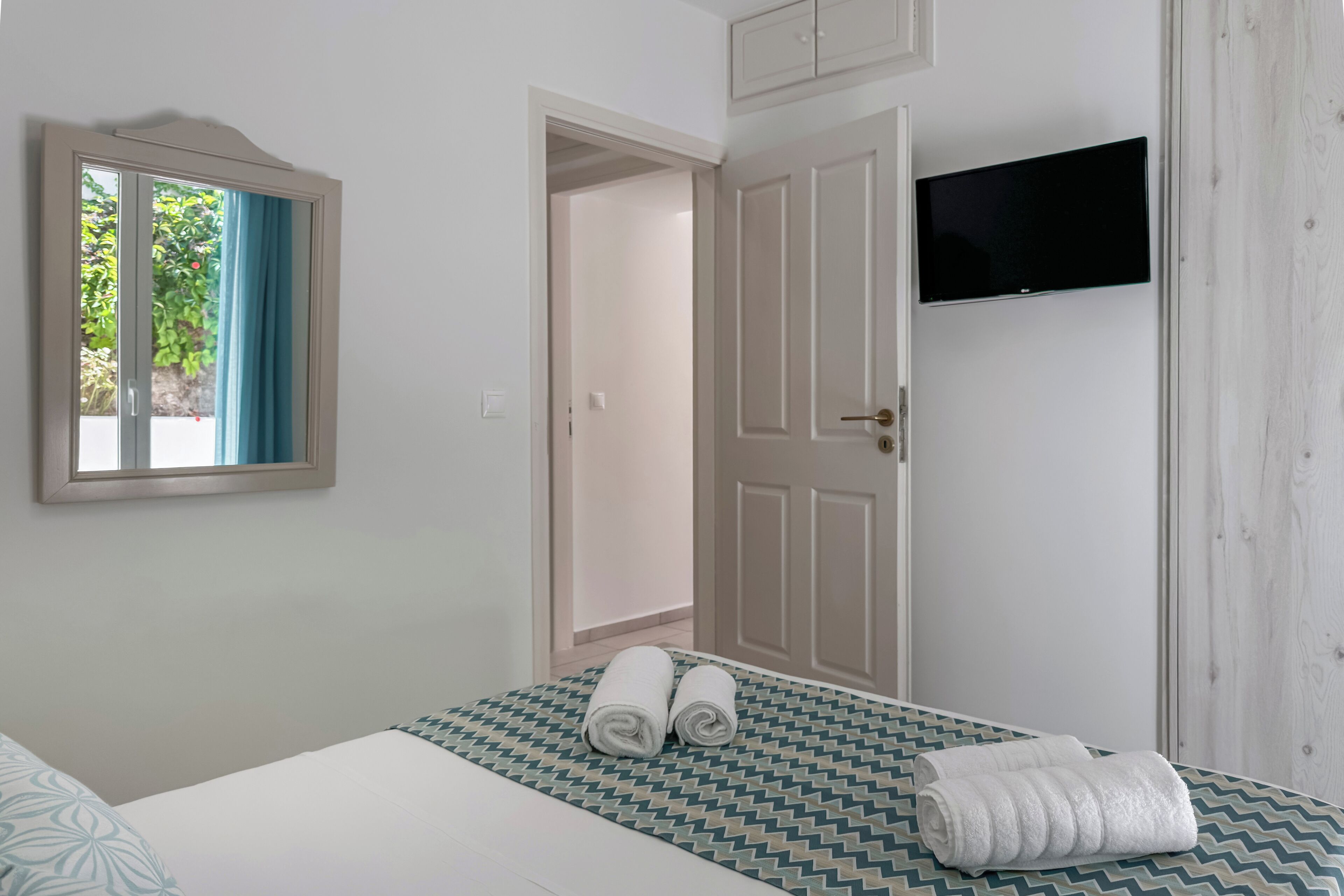 A hotel room with a bed, a TV mounted on the wall, and a door leading to another room.