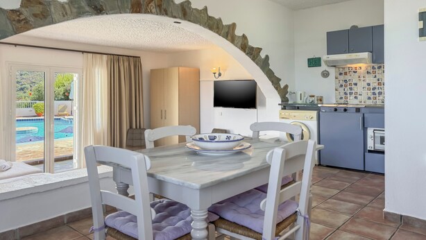A dining area with a stone arch, a TV, and a kitchen with blue cabinets. - Pano Stalos (Chania)