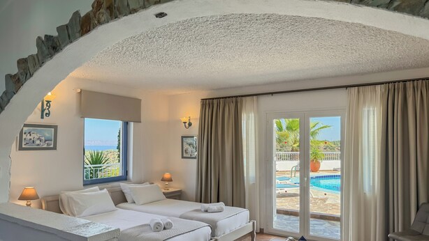 A bedroom with two beds, a bench, a small table, and a view of a swimming pool. - Pano Stalos (Chania)