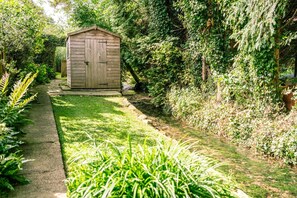 Stroll along the serene garden pathway to a charming shed surrounded by lush greenery.