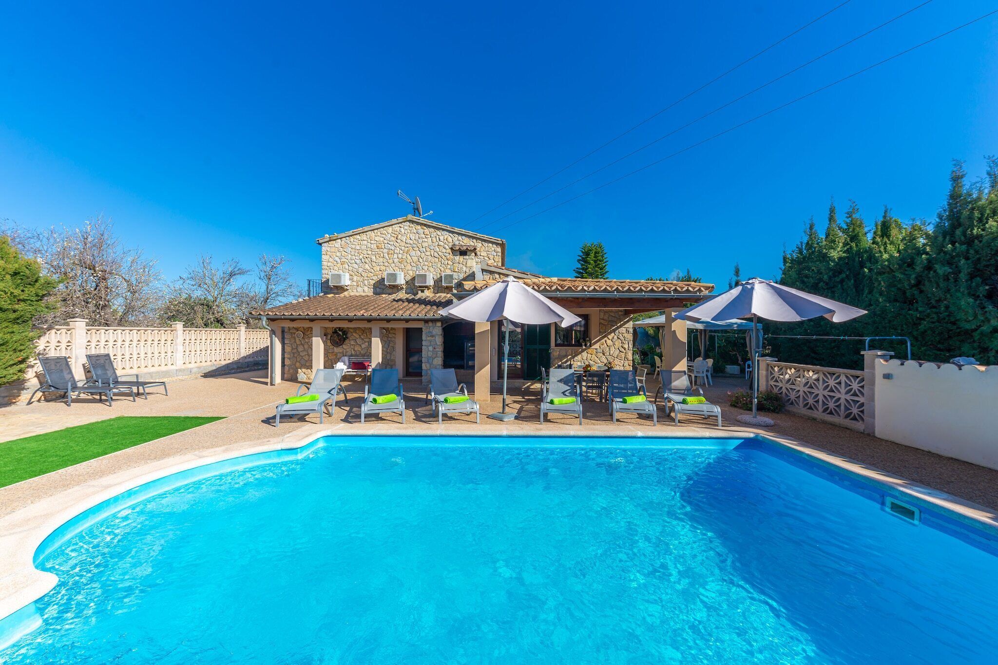 A swimming pool with lounge chairs and umbrellas, surrounded by a stone building with a tiled roof.