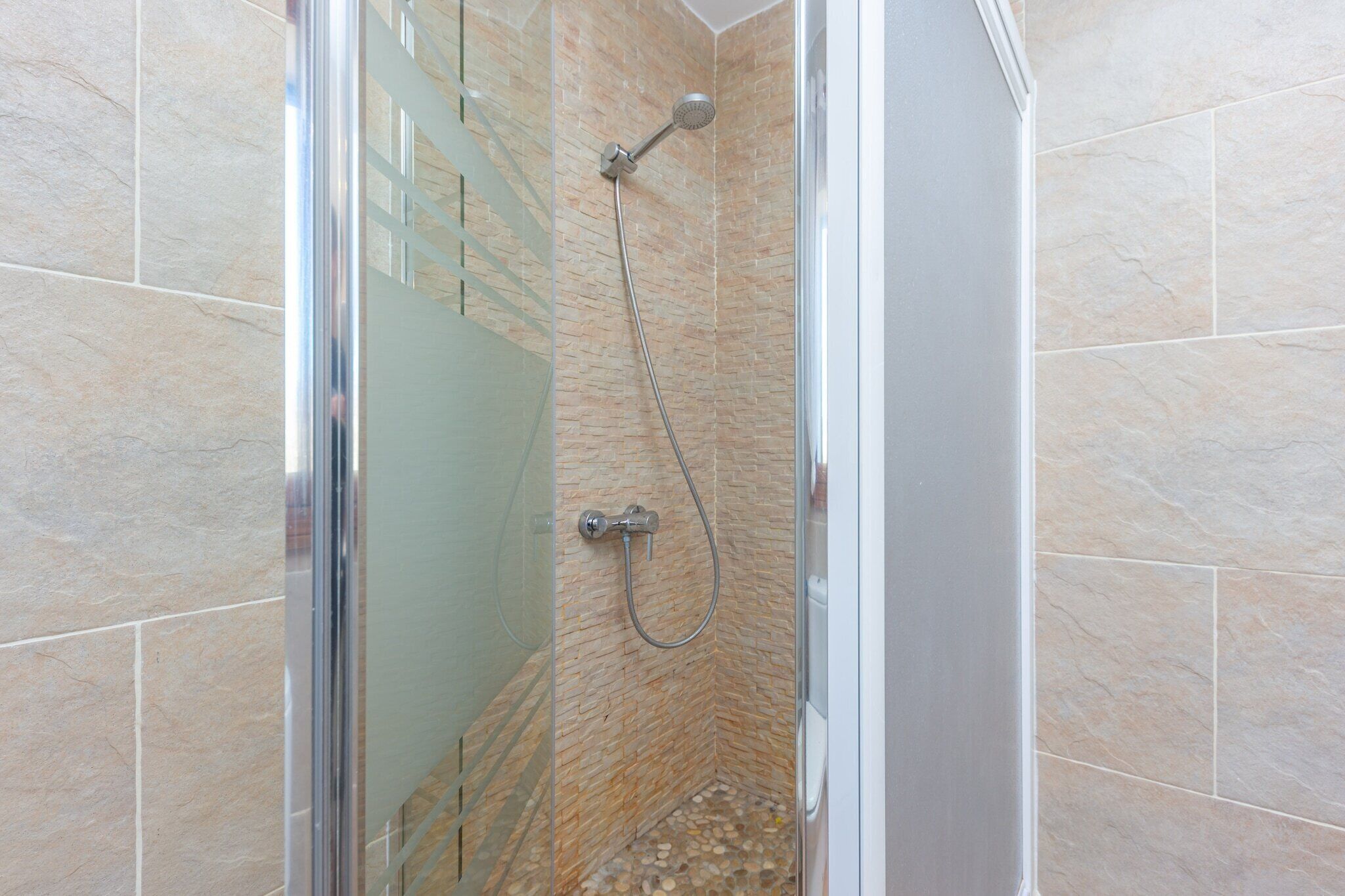 Een douchecabine met glazen wanden, een handdouche en een kraan op de muur.