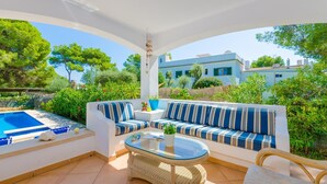 A sunlit outdoor patio with a pool, a wicker table, and striped sofas. - Ca N'estel - Villa With Private Pool In Cala D'or (Cala D'or, Illes Balears)