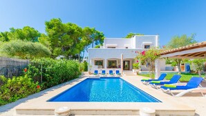 A swimming pool with lounge chairs, a white building, and lush greenery. - Ca N'estel - Villa With Private Pool In Cala D'or (Cala D'or, Illes Balears)