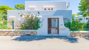A white building with a stone base, a small entrance, and a garden with red flowers. - Ca N'estel - Villa With Private Pool In Cala D'or (Cala D'or, Illes Balears)