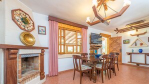 A dining area with a wooden table and chairs, a fireplace, and a large window with curtains. - Els Pins - Villa With Private Pool In Crestatx (Crestatx , Illes Balears)