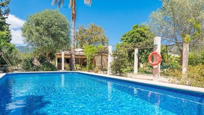 A clear blue swimming pool surrounded by lush greenery and a clear sky.