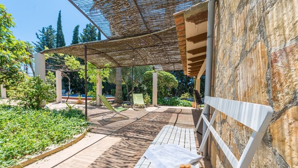 A wooden bench with a bowl of cookies, a pergola, and a stone wall.