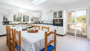 A modern kitchen with white cabinetry, a dining table with blue cushions, and a view to the outside.