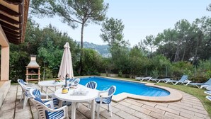 Un espace aménagé au bord de la piscine, avec une table ronde et des chaises, un barbecue et des chaises longues.