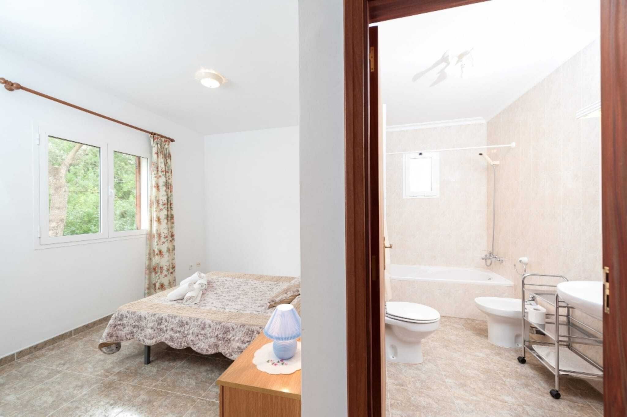 Un dormitorio con cama, mesita de noche y ventana con cortinas. El piso es de baldosas y las paredes son blancas.