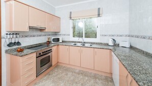 Une cuisine compacte avec des meubles de couleur pêche, un plan de travail en granit, un four encastré, un four à micro-ondes, un évier et une fenêtre donnant sur un espace verdoyant.
