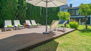 A wooden deck with lounge chairs and a large umbrella, surrounded by greenery and a modern building. - Can Cabrit - Villa With Private Pool In Alaró (AlarÓ, Illes Balears)
