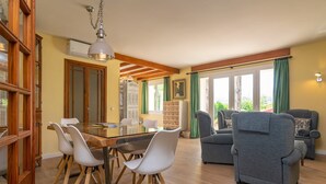 A dining area with a glass table and white chairs, a gray sofa, and wooden beams on the ceiling. - Can Reure - Villa With Private Pool In Inca (Inca, Illes Balears)
