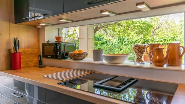 A modern kitchen with a built-in oven, a microwave, and a window overlooking greenery. - Can Reure - Villa With Private Pool In Inca (Inca, Illes Balears)