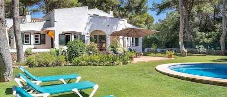 A white villa with a swimming pool, green lawn, and lounge chairs.