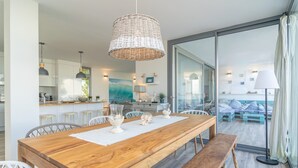 Una cocina moderna con armarios blancos, una mesa de comedor de madera y una lámpara colgante de mimbre.