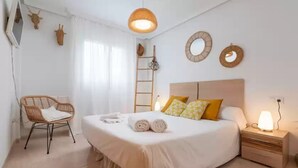 Ett välordnat sovrum med en säng, ett sängbord, en lampa och en stol.