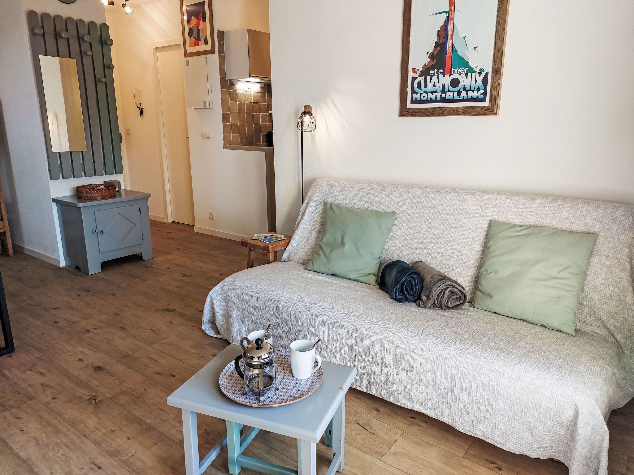 A cozy living room with a sofa, pillows, a coffee table with a coffee pot and cup, a side table, and a framed picture on the wall.