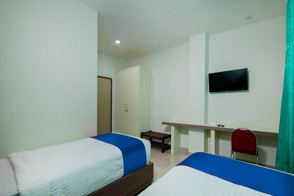 A room with two beds, a TV mounted on the wall, a desk, and a chair.