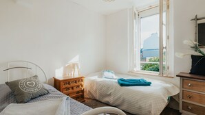 Quarto com duas camas, cômoda de madeira, janela com vista e luminária pendente.